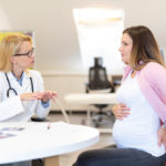Young pregnant woman talking with doctor and having back pain.