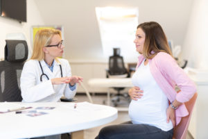 Young pregnant woman talking with doctor and having back pain.