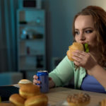 Overweight lady eating unhealthy food, watching show on laptop, sedentary life