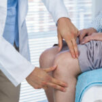 Mid section of doctor examining patient knee in clinic