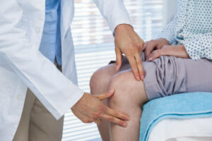 Mid section of doctor examining patient knee in clinic